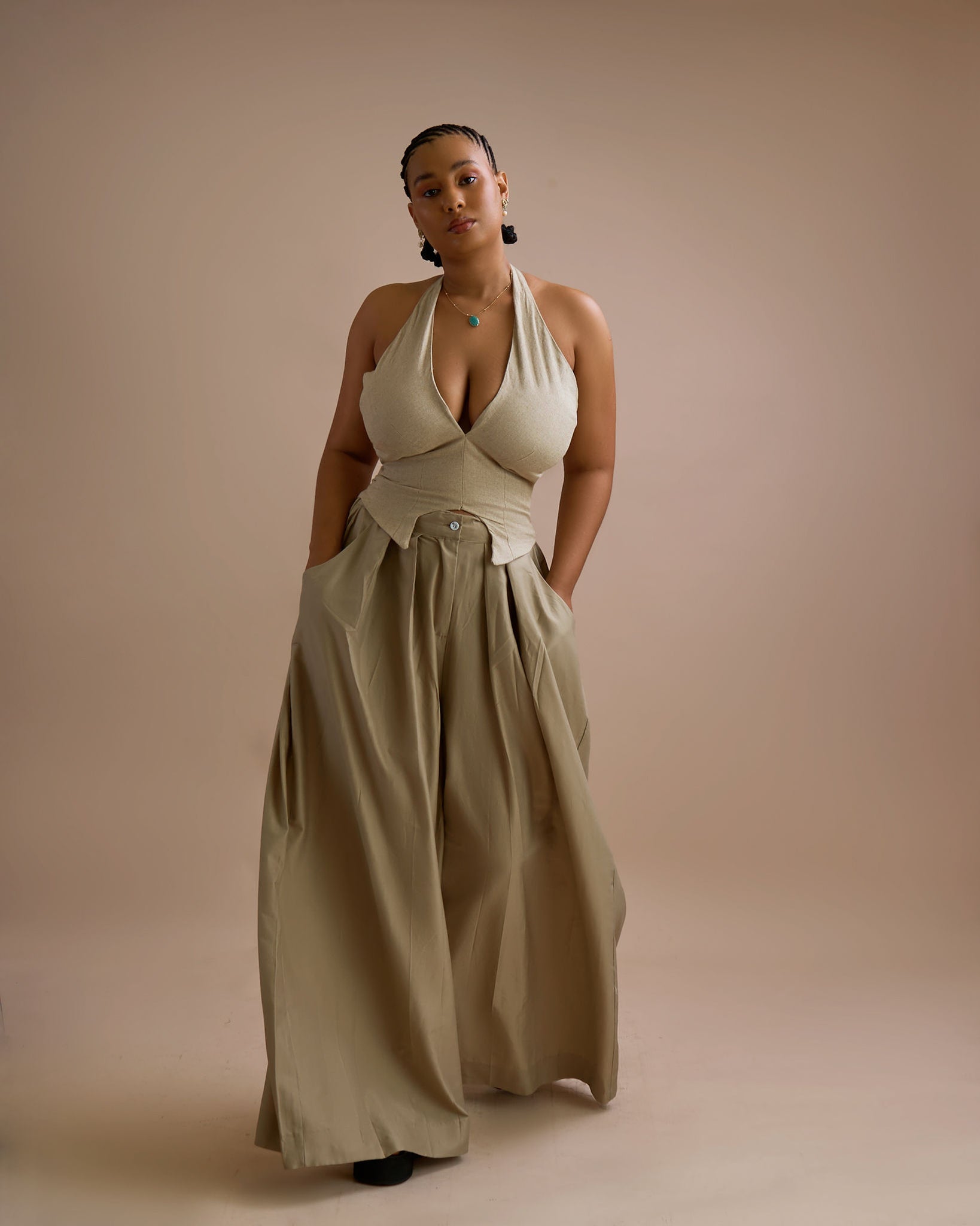 Woman wearing a beige halter top and wide-leg pants against a beige background